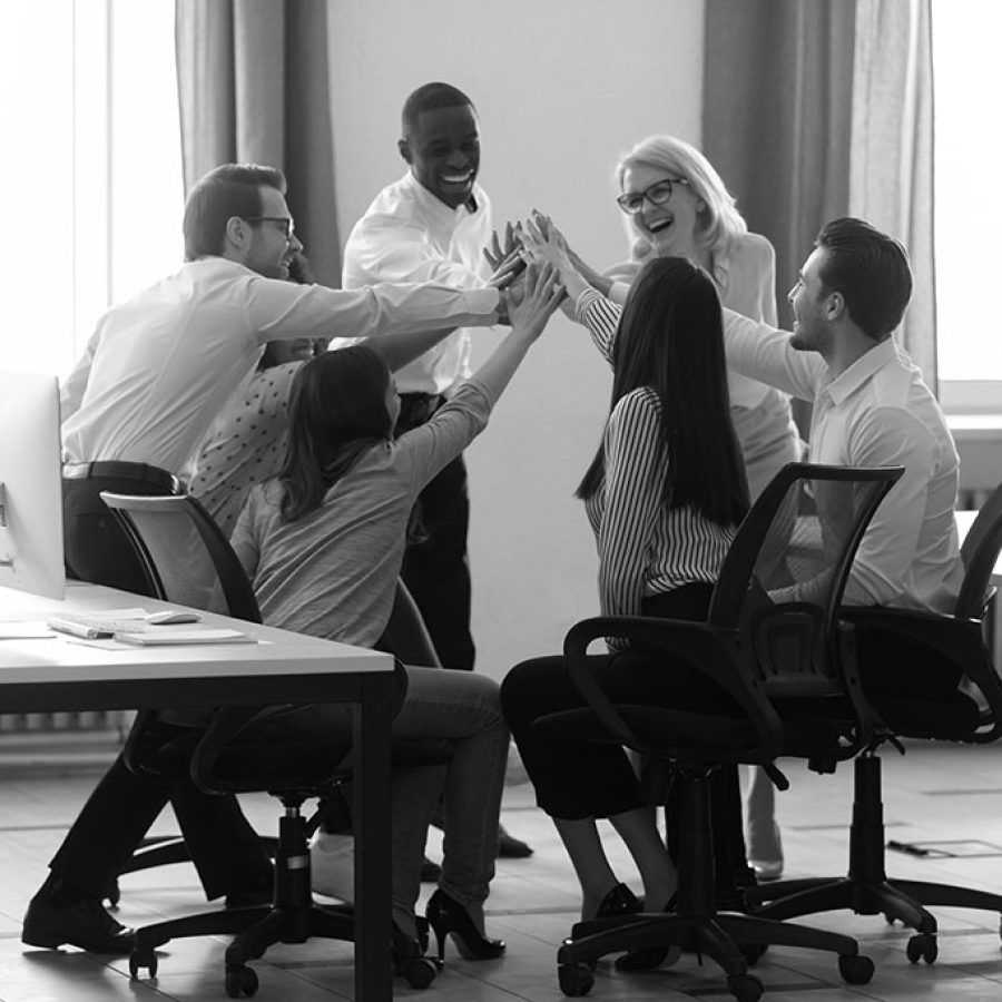 Happy diverse employees sitting in circle, giving high five at business briefing in office, smiling colleagues engaged in team building activity, celebrating achievement, business win or good result
